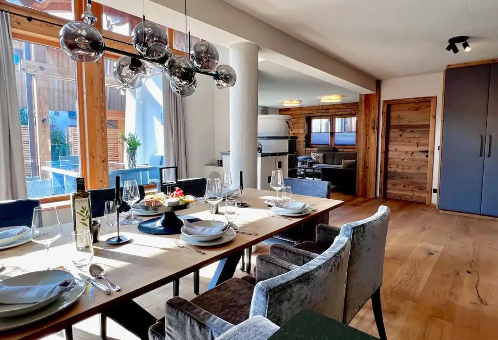 Im hellen Wohn- und Essbereich der Kaiserlodge in Reith bei Kitzbühel steht ein gedeckter Esstisch mit Blick auf die Terrasse und die Holzelemente.