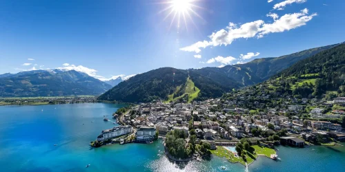 Über Zell am See breitet sich der türkisblaue See vor der Alpenkulisse aus, während die Stadt am Ufer und die Sonne den Himmel klar erleuchten.