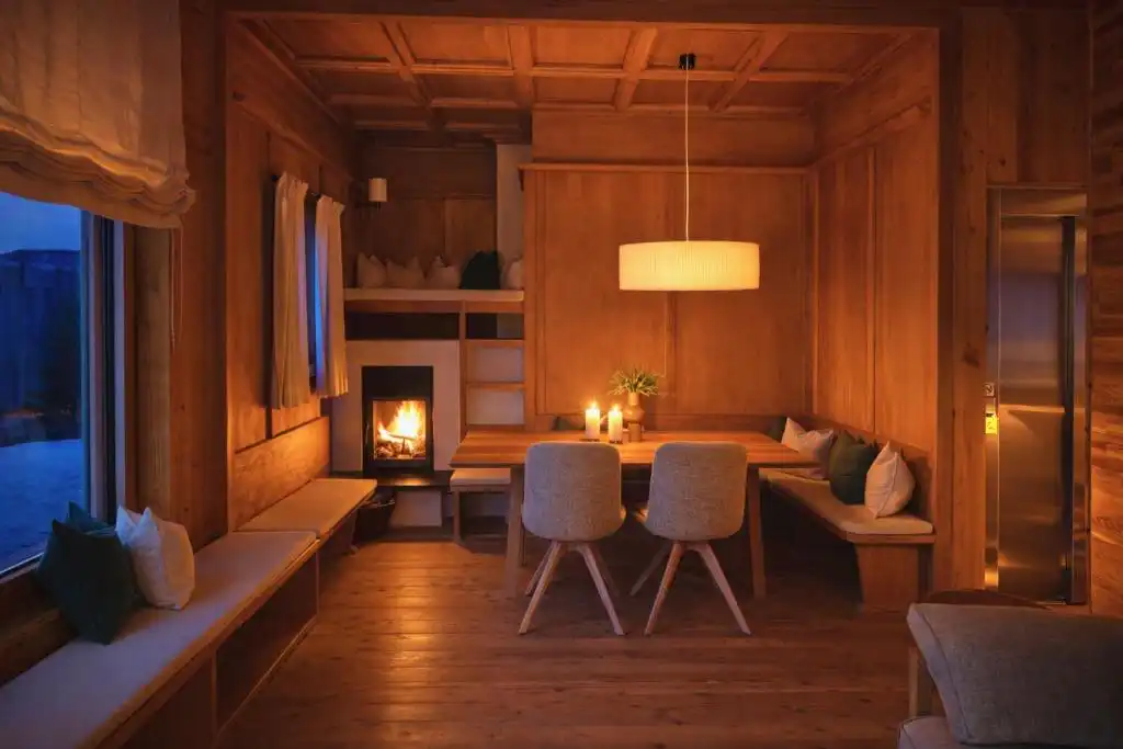 Ein holzverkleideter Essbereich mit Kamin, eingebauten Sitzbänken, Kerzen und Pendelleuchte schafft eine ruhige Atmosphäre am Abend.